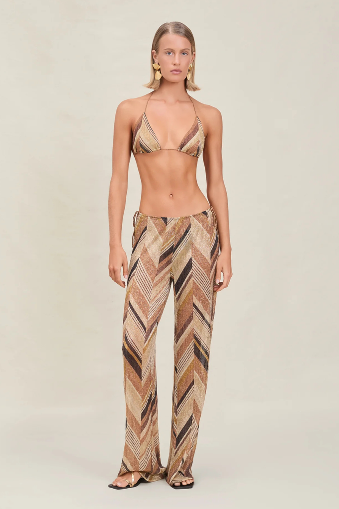 Woman wearing a patterned bikini and pants on a plain background